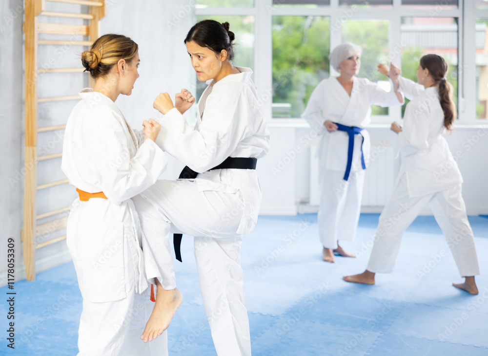 Women in white kimonos are engaged in wrestling at sports training. Woman paired up with female partner performs classic techniques of repelling blow in karate technique Women in white kimonos are engaged in wrestling at sports training. Woman paired up with female partner performs classic techniques of repelling blow in karate technique