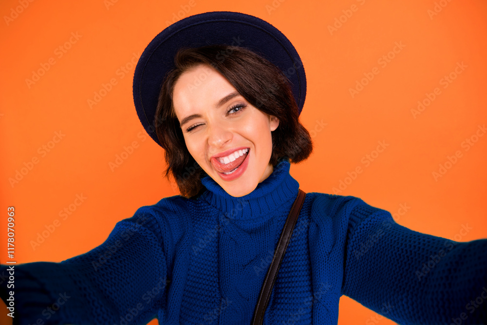 Self photo of winking cute nice friendly fooling girl wearing cap showing her flirty nature while isolated with orange background Self photo of winking cute nice friendly fooling girl wearing cap showing her flirty nature while isolated with orange background