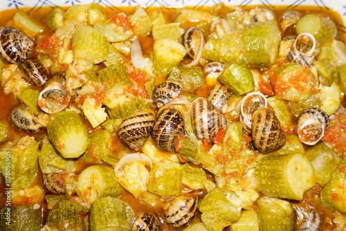 Fototapeta Naklejka Na Ścianę i Meble -  Traditional Cretan food, snails with zucchini in tomato sauce baked in a pot with tomato sauce served on a vintage plate