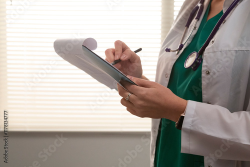 Female doctor writing medical notes on clipboard in hospital room photo