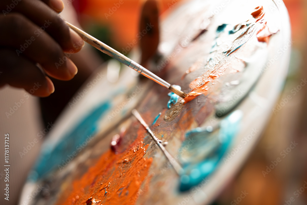 Obraz premium In an art studio, painter mixes multiple watercolor paints on a palette to create a new artwork on canvas. Skilled man painting with tools and showing his imagination, artistic creation. Close up.