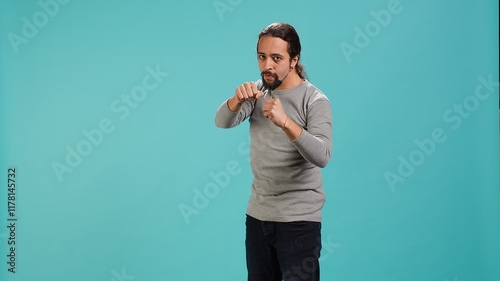 Man pretending to fight, throwing punches, holding defensive guard. Martial artist person doing mock boxing, holding combat stance, exercising, isolated over studio background, camera A photo