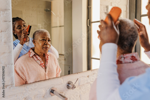 Caregiver brushing hair of elderly woman in bathroom photo