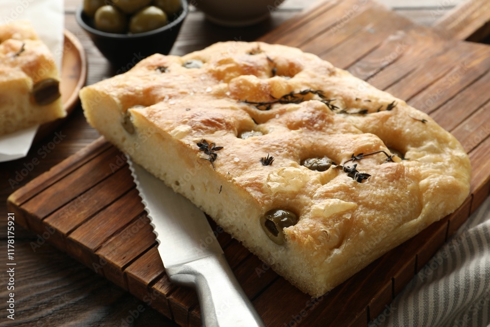 Piece of delicious focaccia bread with olives, thyme, salt and knife on wooden table, closeup Piece of delicious focaccia bread with olives, thyme, salt and knife on wooden table, closeup