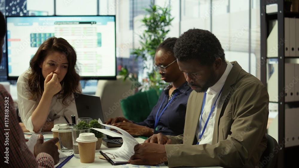 Fototapeta premium Shareholder examining infographics and resource allocation on tablet, gathering with associates for a strategy session. Utilizing data analytics to develop innovative solutions for growth. Camera B.