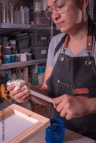 Young white-skinned Latina woman doing printing work using the screen printing and printing with meshes method. It could be for industry or sales. Advertising uses different tools or objects. She is h photo