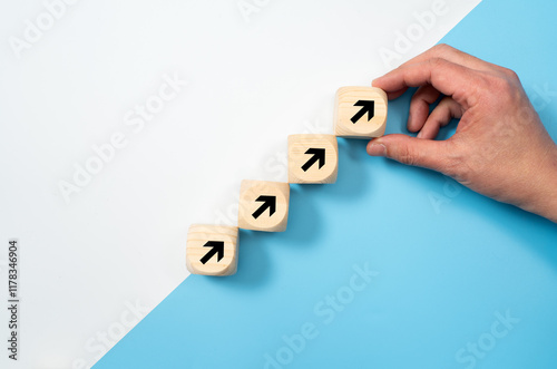 Hand placing wooden blocks with arrows pointing upwards for business, sales, revenue or investment growth concept isolated on white and blue background