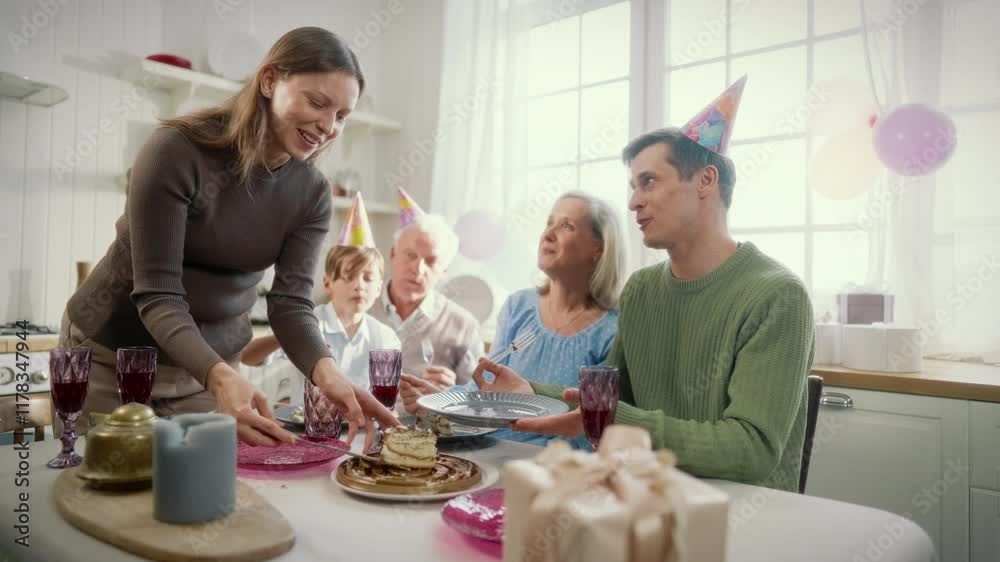 Woman putting piece of cake on plate of her husband in family birthday party. Happy people celebrating anniversary, sitting together on home kitchen in cozy light interior, slow motion shot, eating