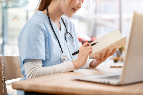 A close-up of a beautiful female medical student in scrubs reading her lecture book in the library.