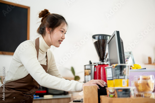 A smiling Asian female barista is working on a computer at the cashier checkpoint at the counter. photo