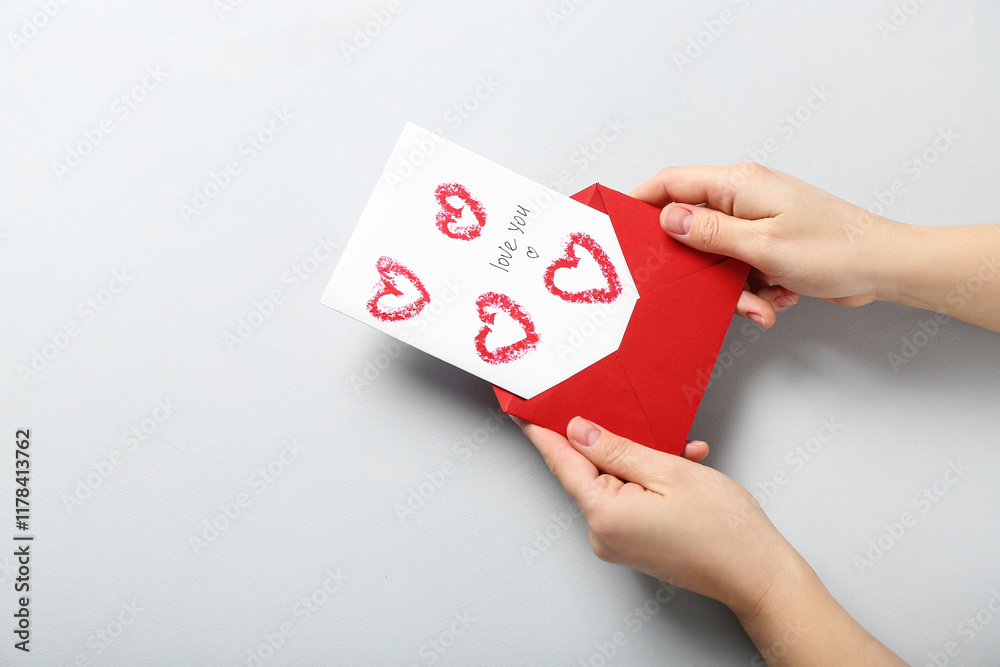 Female hands with red envelope and greeting card on grey background, closeup. Valentine's Day celebration Female hands with red envelope and greeting card on grey background, closeup. Valentine's Day celebration