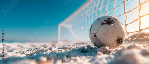 Soccer Ball Resting on Sandy Beach Near Goalpost Under Bright Sunlight with Clear Blue Sky