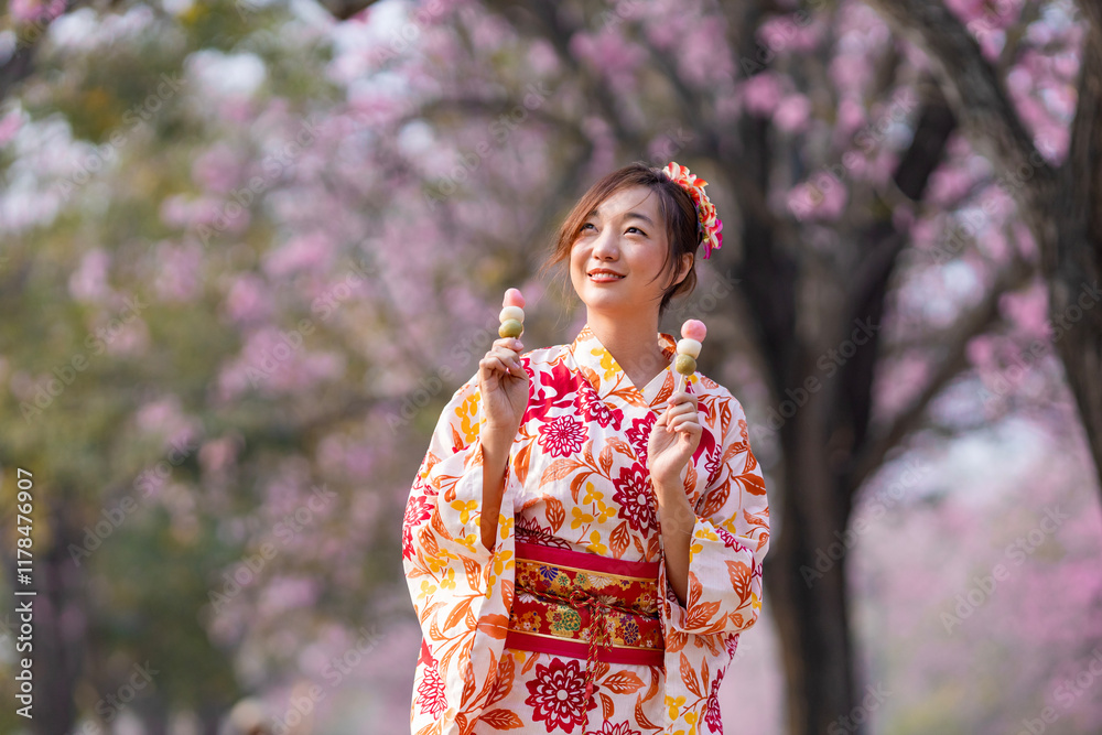 Japanese woman in traditional kimono dress holding sweet hanami dango dessert while walking inside park at cherry blossom tree during spring sakura festival Japanese woman in traditional kimono dress holding sweet hanami dango dessert while walking inside park at cherry blossom tree during spring sakura festival