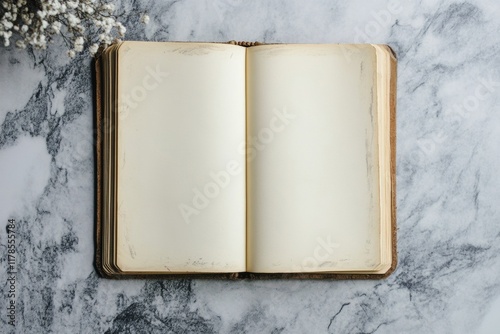 Book is open to a blank page. The book is on a marble countertop. The book is old and has a leather binding