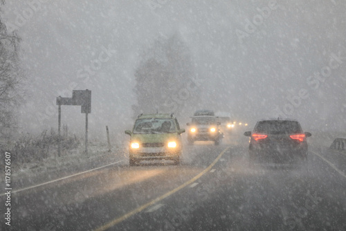 Driving in highway traffic with winter sleet and snow creating low visibility conditions, facing bright headlights of the oncoming traffic.