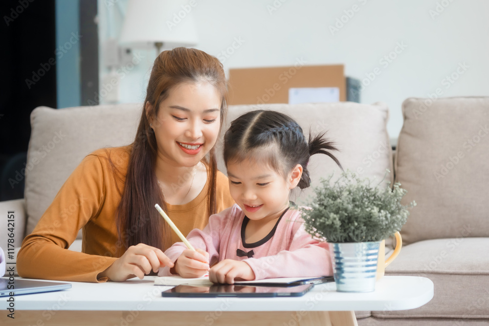 Asian young mother and her daughter sit together on the sofa in the cozy living room, working on homework at the desk, creating a warm and supportive atmosphere for learning, love, hug, mother days. Asian young mother and her daughter sit together on the sofa in the cozy living room, working on homework at the desk, creating a warm and supportive atmosphere for learning, love, hug, mother days.