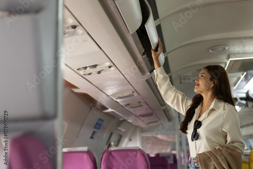 A woman is looking up at the air vent in an airplane. She is holding a cell phone and a backpack photo