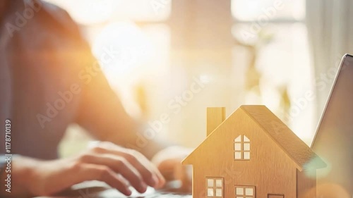 A close-up of a wooden house model with stacked coins symbolizing property investment and financial planning. A laptop and business documents in the background emphasize the digital and analytical