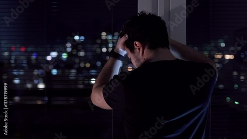 Depressed man standing by the window at night