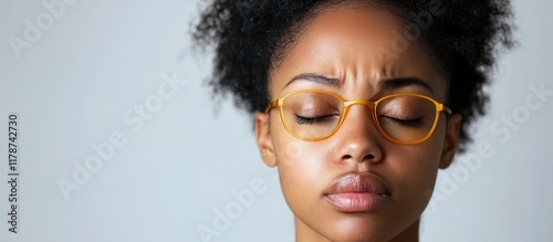 Sleep deprived young African American woman with dark circles under eyes expressing fatigue against a soft grey background with empty text space