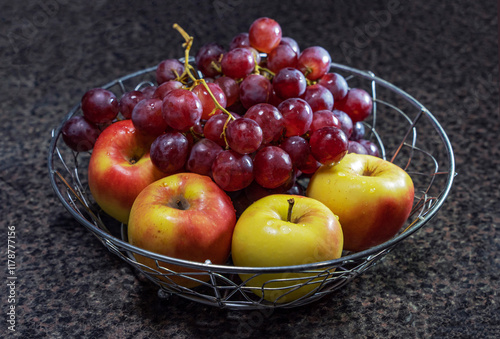 In a metal fruit bowl there are four freshly washed apples and two branches of large red grapes, fruits of late ripening varieties. photo