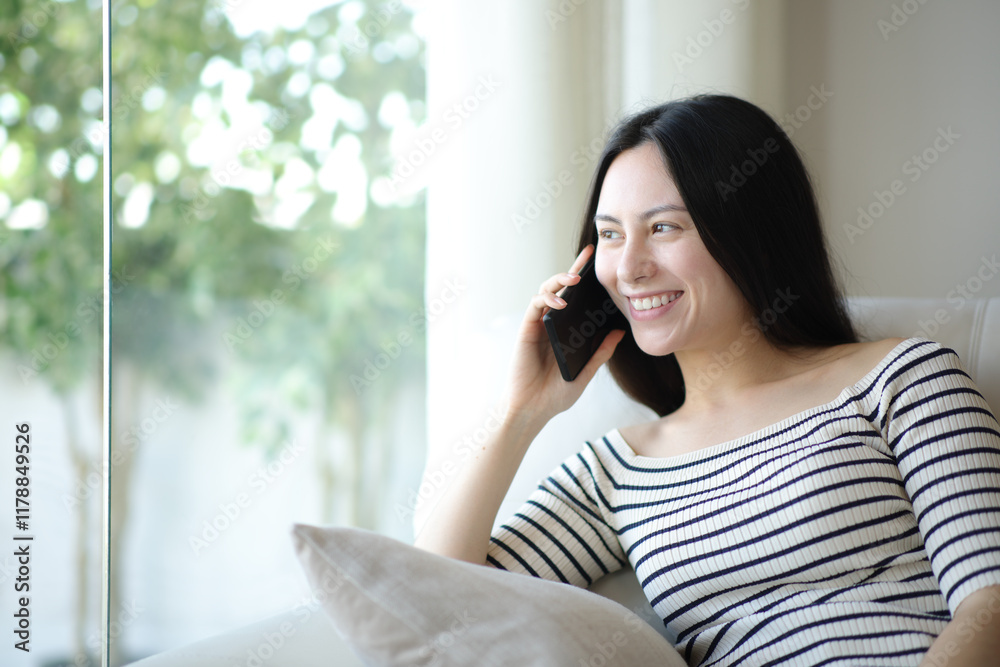 Happy asian woman talking on phone looking through a window