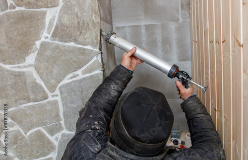 Fotografie A man is fixing a wall with a tube of caulk