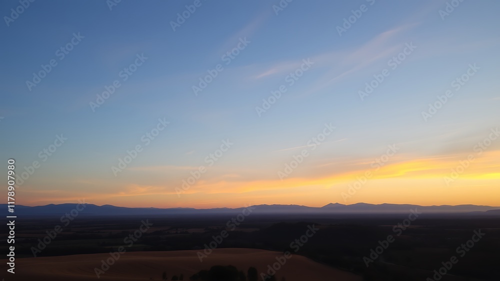 Obraz premium Serene sunset over rolling hills and distant mountains, a peaceful landscape panorama, captivating golden hour light,