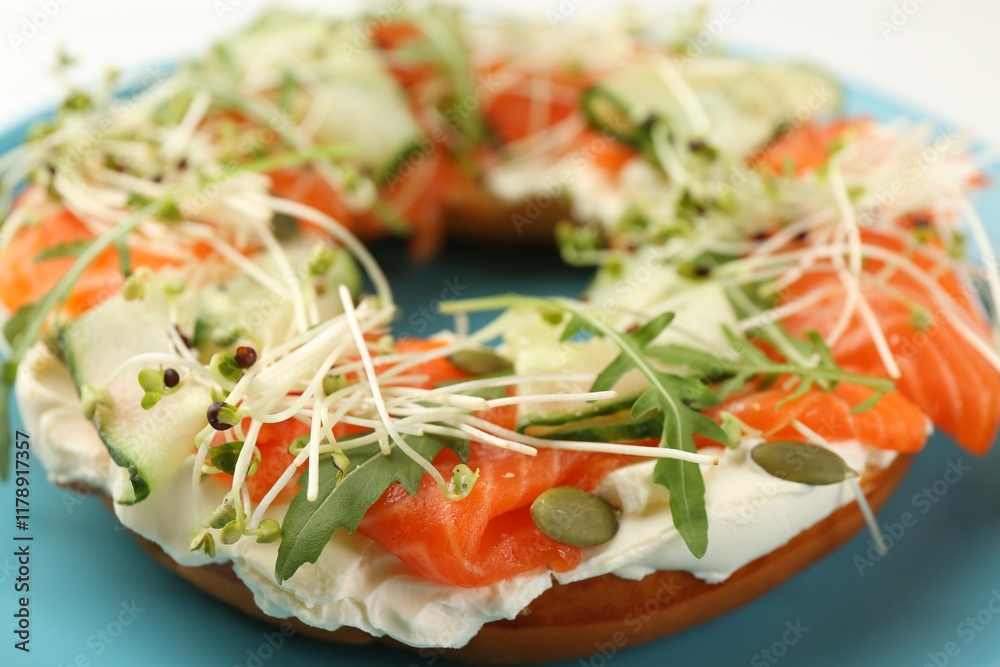 Half of delicious bagel with salmon, microgreens, arugula and cream cheese on plate, closeup Half of delicious bagel with salmon, microgreens, arugula and cream cheese on plate, closeup