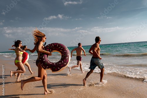 Group of happy young friends are having fun and runs to swim at the beach. Group of tourists with inflatable rings at sunset sea