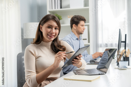 Smiling beautiful woman holding tablet to recheck list, looking at camera photo shooting portrait business pose profile while working with smart coworker at modern office at morning time. Postulate. photo