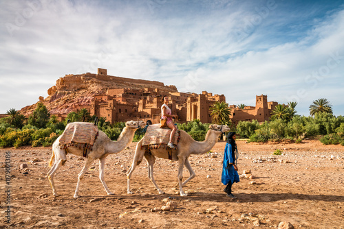 Woman riding a camel in front of old fortified town, Ait Benhaddou, Morocco