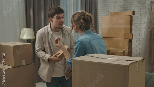 Young couple moving into new apartment, space filled with cardboard boxes, man and woman standing in the room, start arguing about new apartment, upset negative expression.