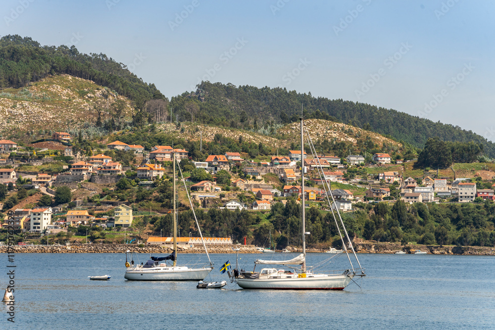Boats by the coast on Marina of Moana with residential houses in the background, Galicia, Spain