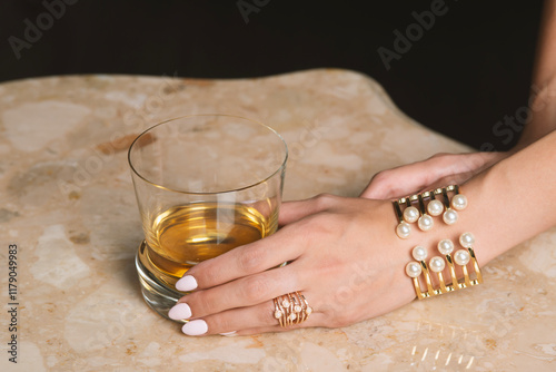 female hand with golden bracelet holding glass of whiskey
