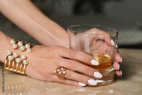 female hand with golden bracelet holding glass of whiskey
