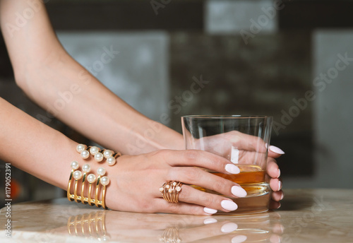 female hand with golden bracelet holding glass of whiskey