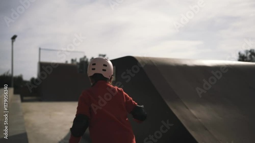 A cheerful child in a helmet and protective gear smiles at the camera in a skatepark setting. photo