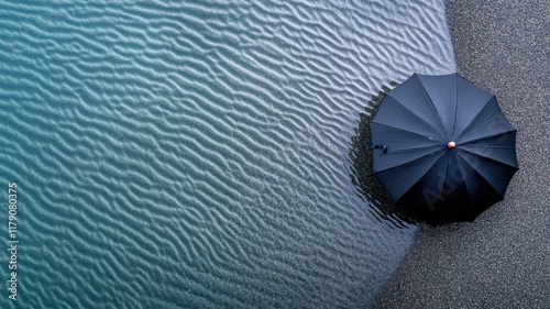Open umbrella sits on pebbly beach near gently rippling blue water