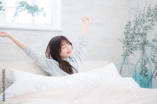 ベッドの上で寝起きで伸びやストレッチをする女性 photo