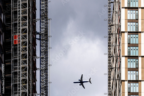 This dramatic image portrays an airplane flying through a narrow gap between towering buildings, symbolizing the intersection of technology and urban architecture in London UK photo