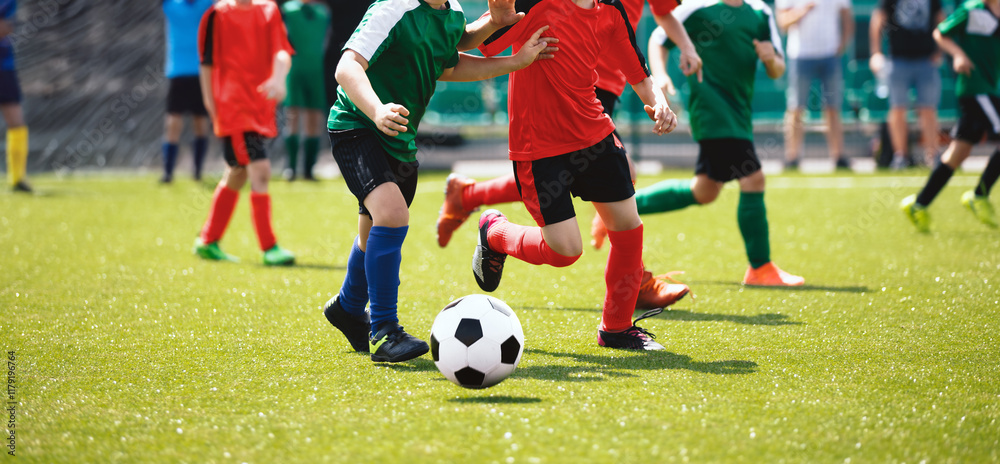 Obraz premium Football soccer match for children. Boys in red and green shirts playing football game on school tournament. Dynamic, action picture of kids competition during playing football. Sport background image