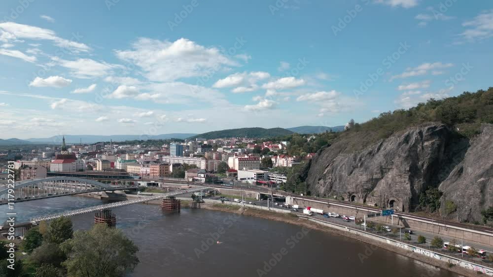 Scenic view of a city Ustí nad Labem with an Elbe river, a bridge, and a rocky hill under a partly cloudy sky Scenic view of a city Ustí nad Labem with an Elbe river, a bridge, and a rocky hill under a partly cloudy sky