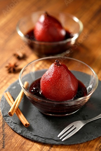 Elegant presentation of poached pears in red wine with cinnamon sticks on a slate plate.