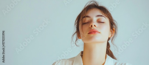 Studio portrait of serene young woman with natural makeup and closed eyes in white clothing against soft pale background with ample copyspace for text photo