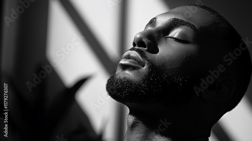 Black and white close-up portrait of a serene young man with eyes closed, illuminated by sunlight.