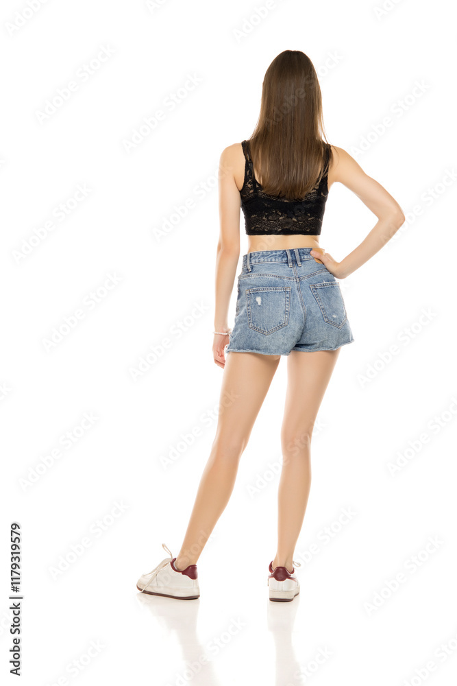 Young woman in a short blue jeans and black sleeveless shirt on a white studio background. Back, rear view. Young woman in a short blue jeans and black sleeveless shirt on a white studio background. Back, rear view.
