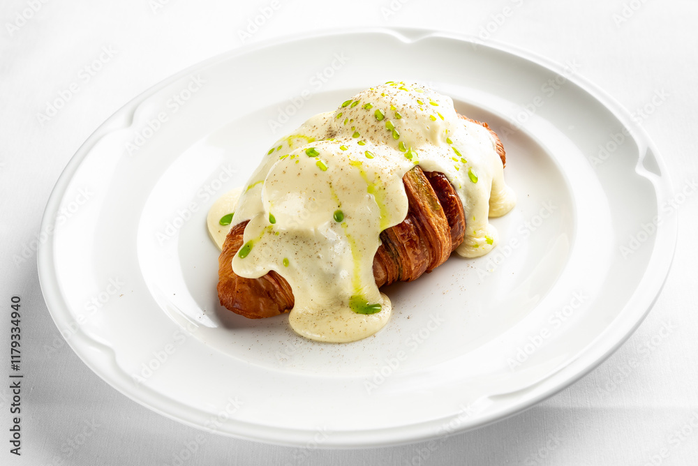 A delicious croissant topped with creamy hollandaise sauce and garnished with green onions on a white plate. Perfect for a gourmet breakfast or brunch setting. A delicious croissant topped with creamy hollandaise sauce and garnished with green onions on a white plate. Perfect for a gourmet breakfast or brunch setting.