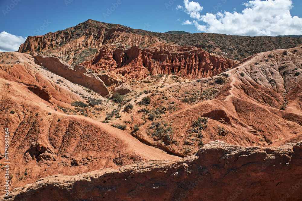 Fototapeta premium Striking landscape features expansive hills with vibrant hues of red, orange, tan, characteristic of desert environment. terrain is rugged and undulating, natural scene, Fairy Tale canyon, Kyrgyzstan