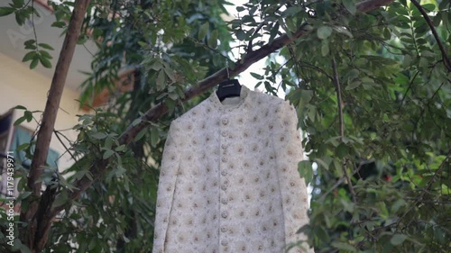 Indian groom`s traditional wedding sherwani hanging on a tree branch. photo